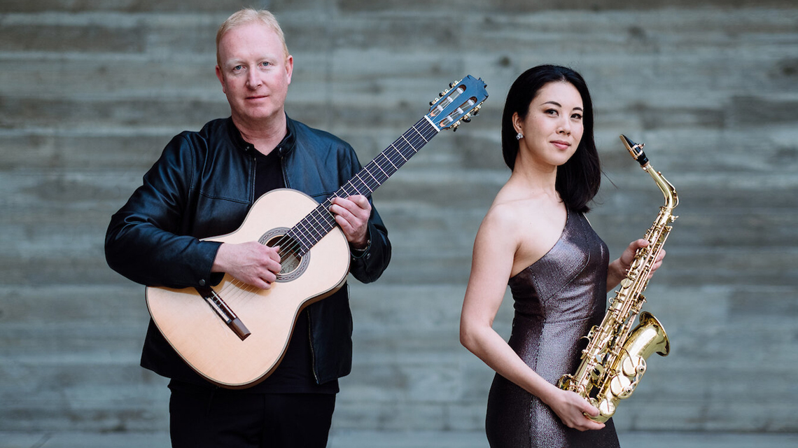 Scott Morris holding guitar and Chika Inoue holding a saxaphone