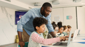Teacher instructing schoolchildren at computers