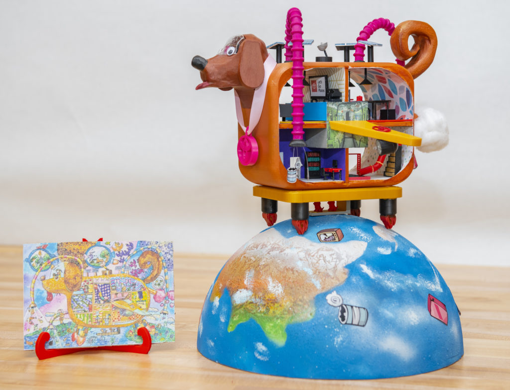 A 3D-printed model of the earth, with images of trash on it. Sitting on top of the ear is a dog-shaped car with rooms inside. Next to the model is the child's drawing that inspired it.
