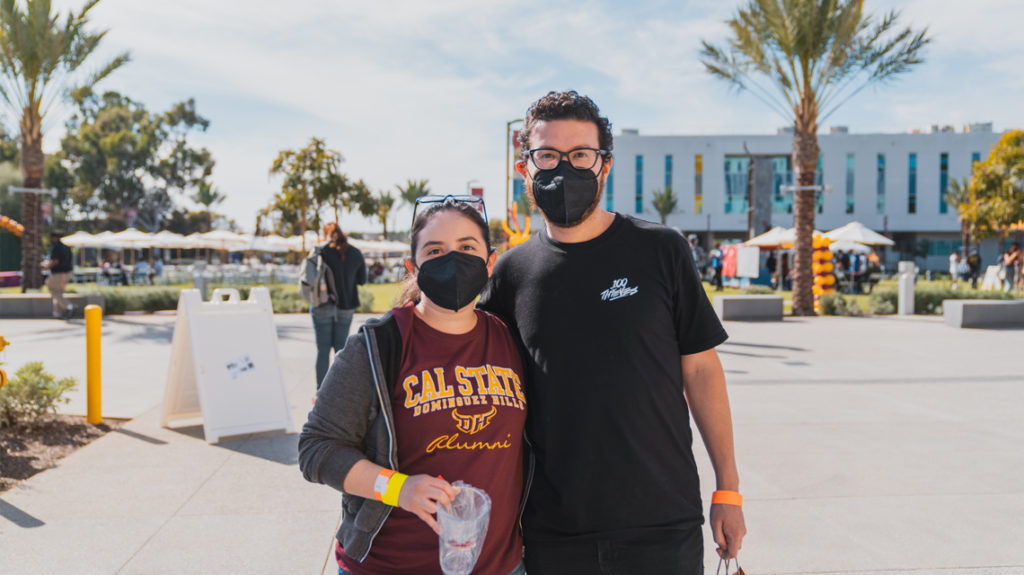 two people, one wearing a CSUDH Alumni shirt, pose for a picture on the CSUDH campus