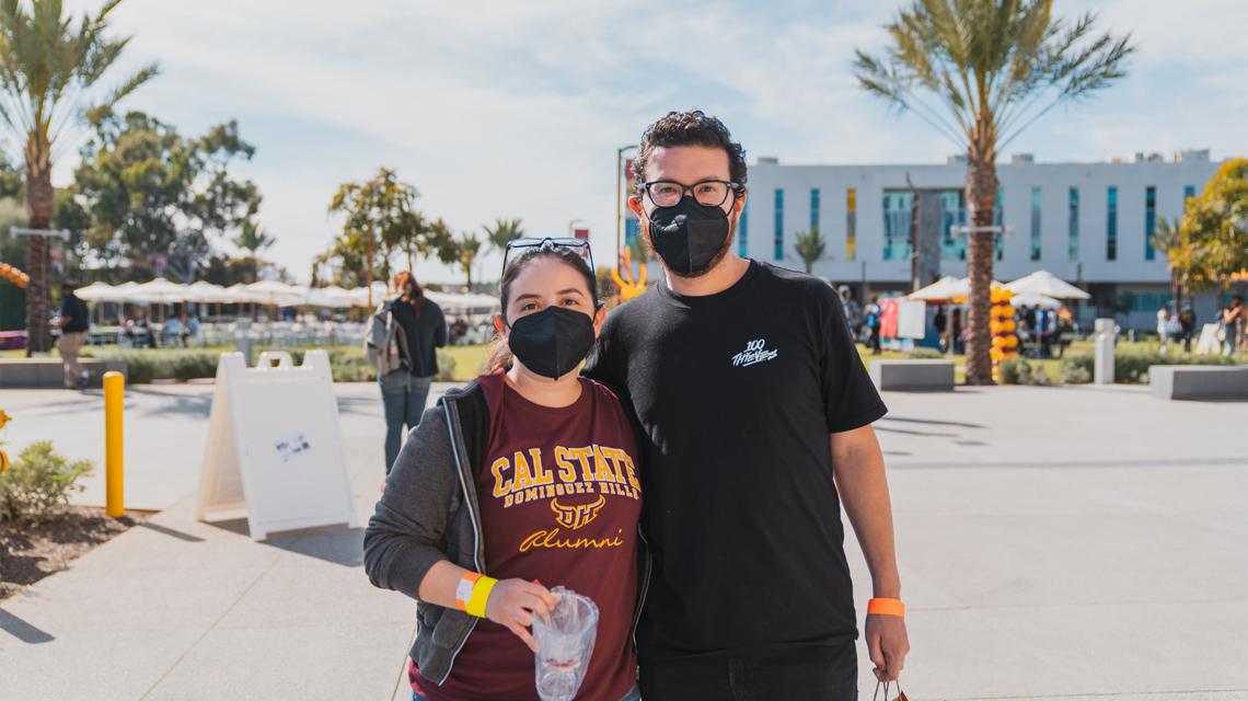 two people, one wearing a CSUDH Alumni shirt, pose for a picture on the CSUDH campus