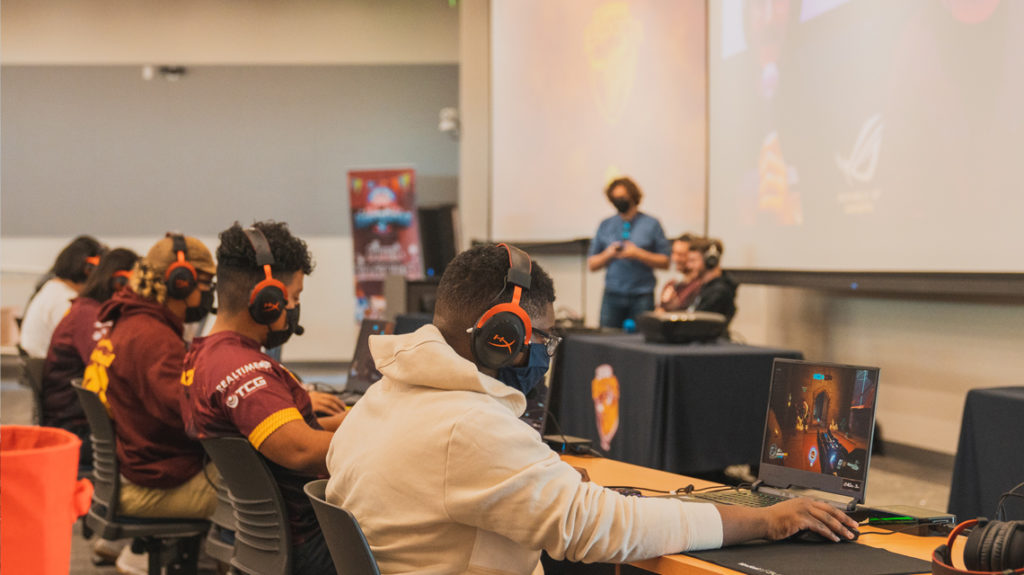 five people with headsets on play video games in the Innovation and Instruction building auditorium