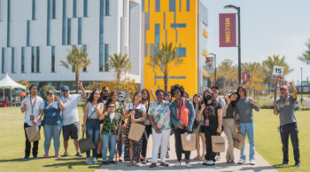 20 people on a tour of campus stand on the CSUDH North Lawn with the Innovation and Instruction buildign behind them.