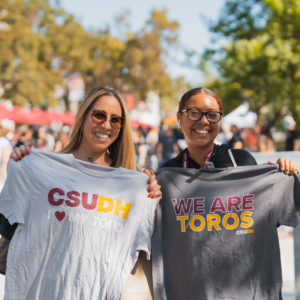 Two people each hold a Tshirt, one saying CSUDH I [heart] My Toro, the other saying We are Toros
