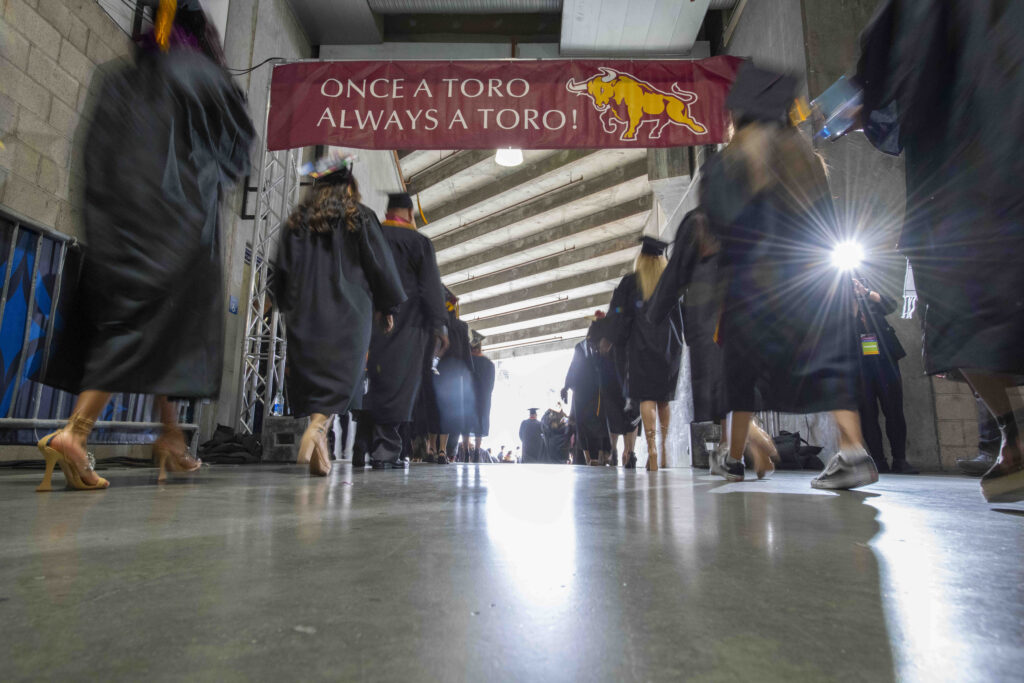 Graduates walking under a sign which says "once a Toro, always a Toro."