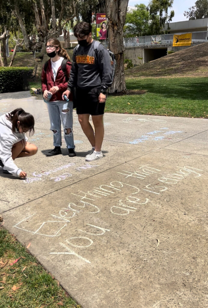 students write with chalk on the sidewalk around the CSUDH Sculpture Garden