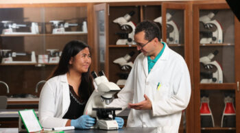 Two people wearing white lab coats in a laboratory, with a microscope