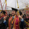Jeisson and other graduates celebrating under ribbons at Commencement