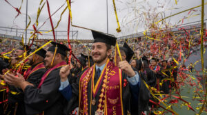 Jeisson and other graduates celebrating under ribbons at Commencement