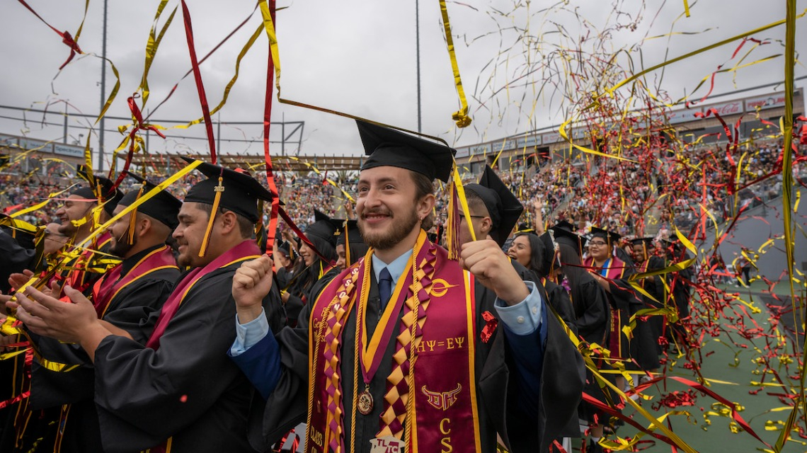 Jeisson and other graduates celebrating under ribbons at Commencement