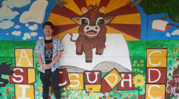 Muralist in front of new CDC mural depicting baby Teddy, an open book, CSUDH, and a sunrise