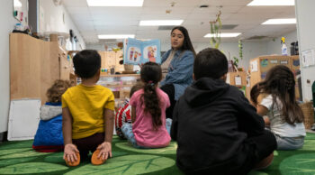 Teacher reads story to seated young children.
