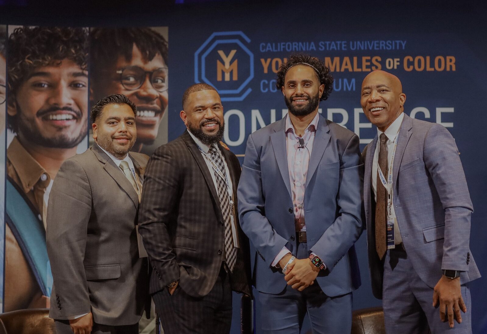 Four men smiling in front of YMOC Conference banner