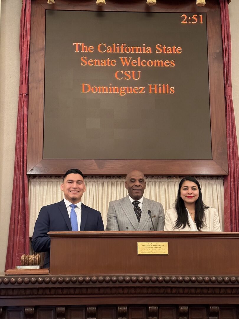 Edgar Mejia-Alezano, State Senator Steve Bradford, and Adilene Tinoco in front of a sign stating "The California State Senate Welcomes CSU Dominguez Hills"
