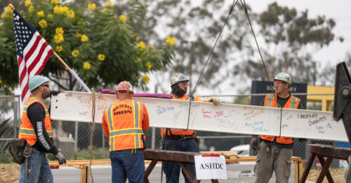 Construction workers hoisting up a metal beam with an American flag on the end