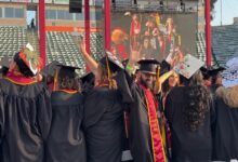 J.D. Elson in regalia waving at Commencement