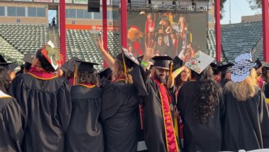 J.D. Elson in regalia waving at Commencement