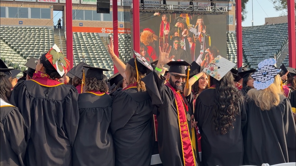 J.D. Elson in regalia waving at Commencement