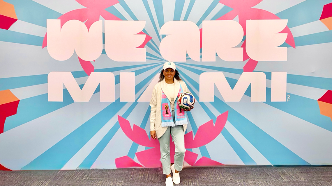 CSUDH Alumna Vanessa Williams Brooks stands in front of a large World Cup banner in Miami, Florida.